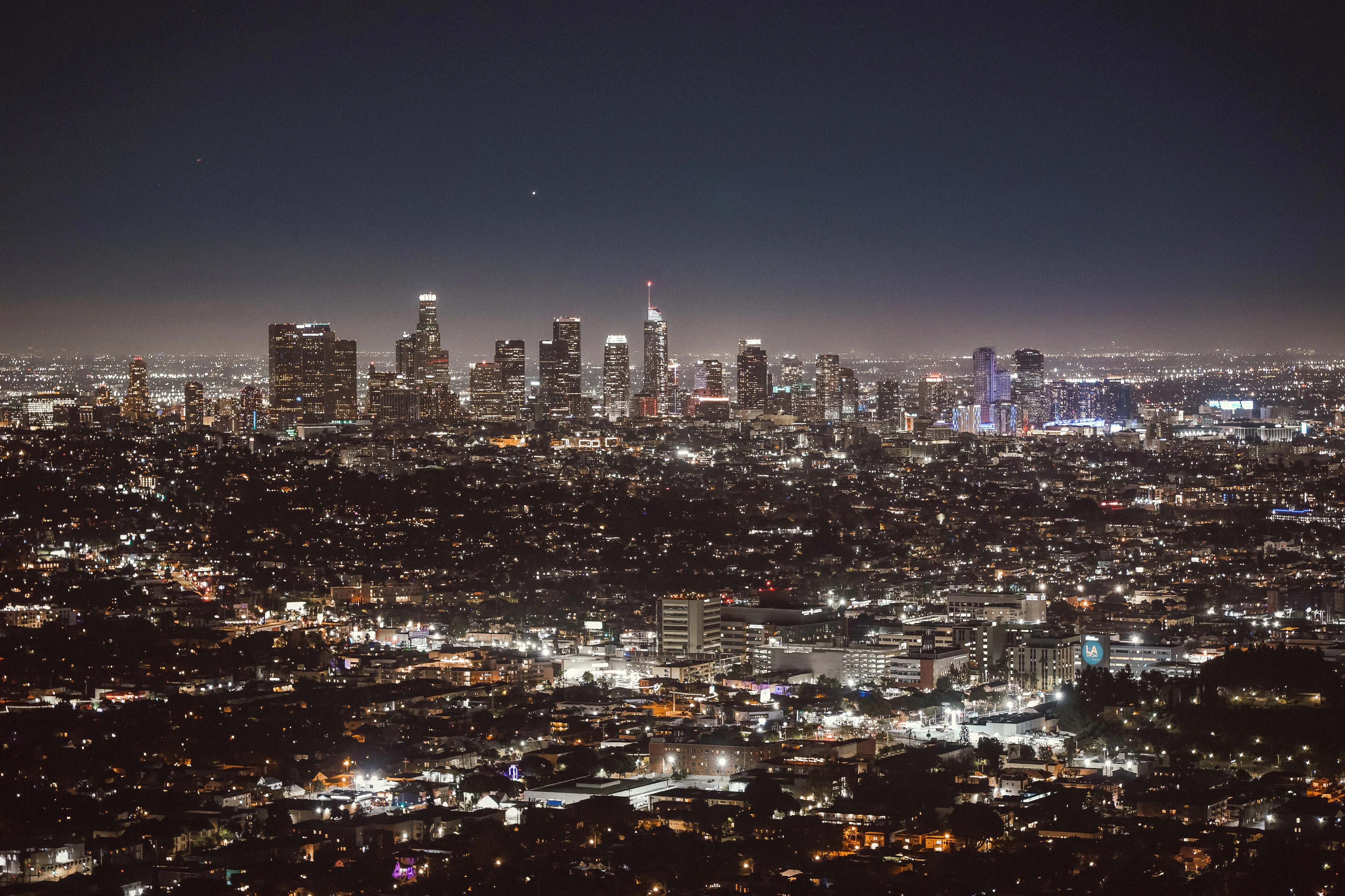A wide network of illuminated streets and buildings leads toward distant towers beneath a dark sky.