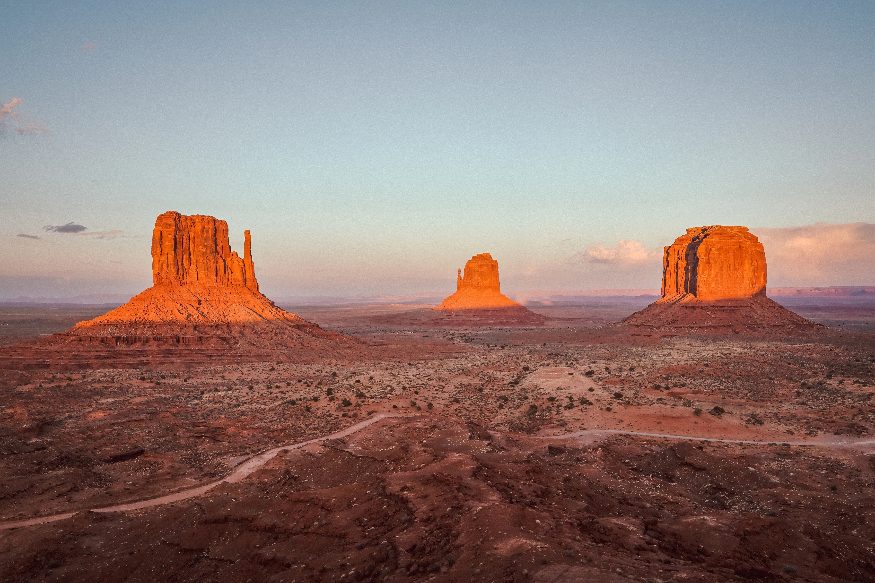 Three separated red rock masses rise from a broad plain, with a curving road in the foreground.