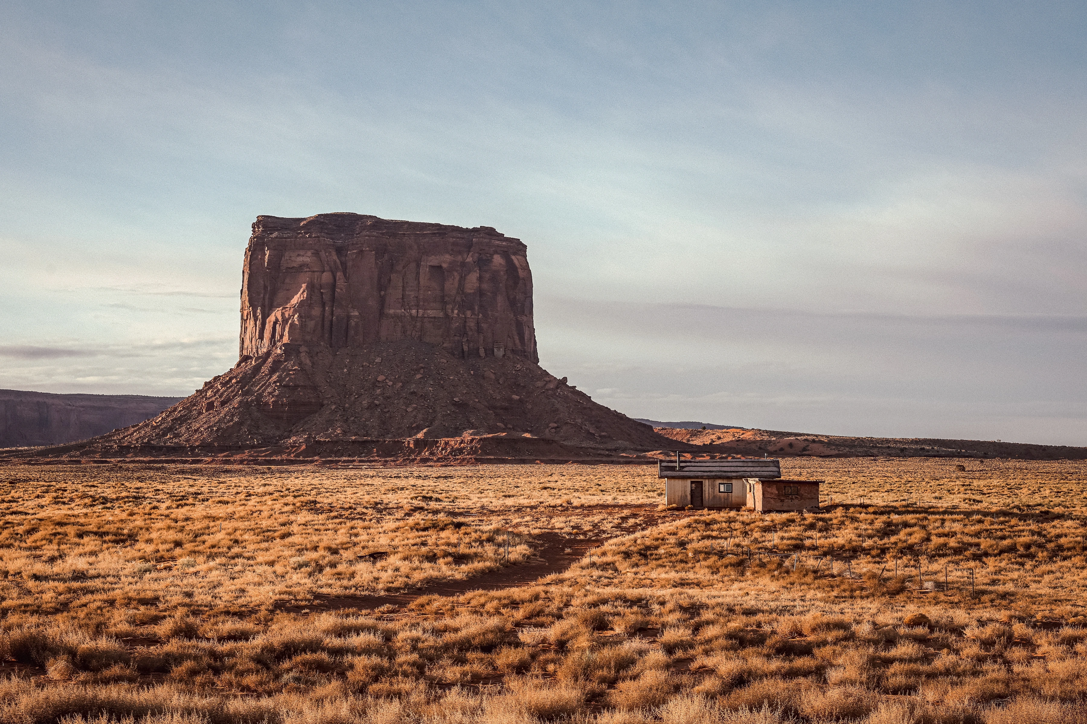 A small building stands beside a large rock formation and a curving dirt track.