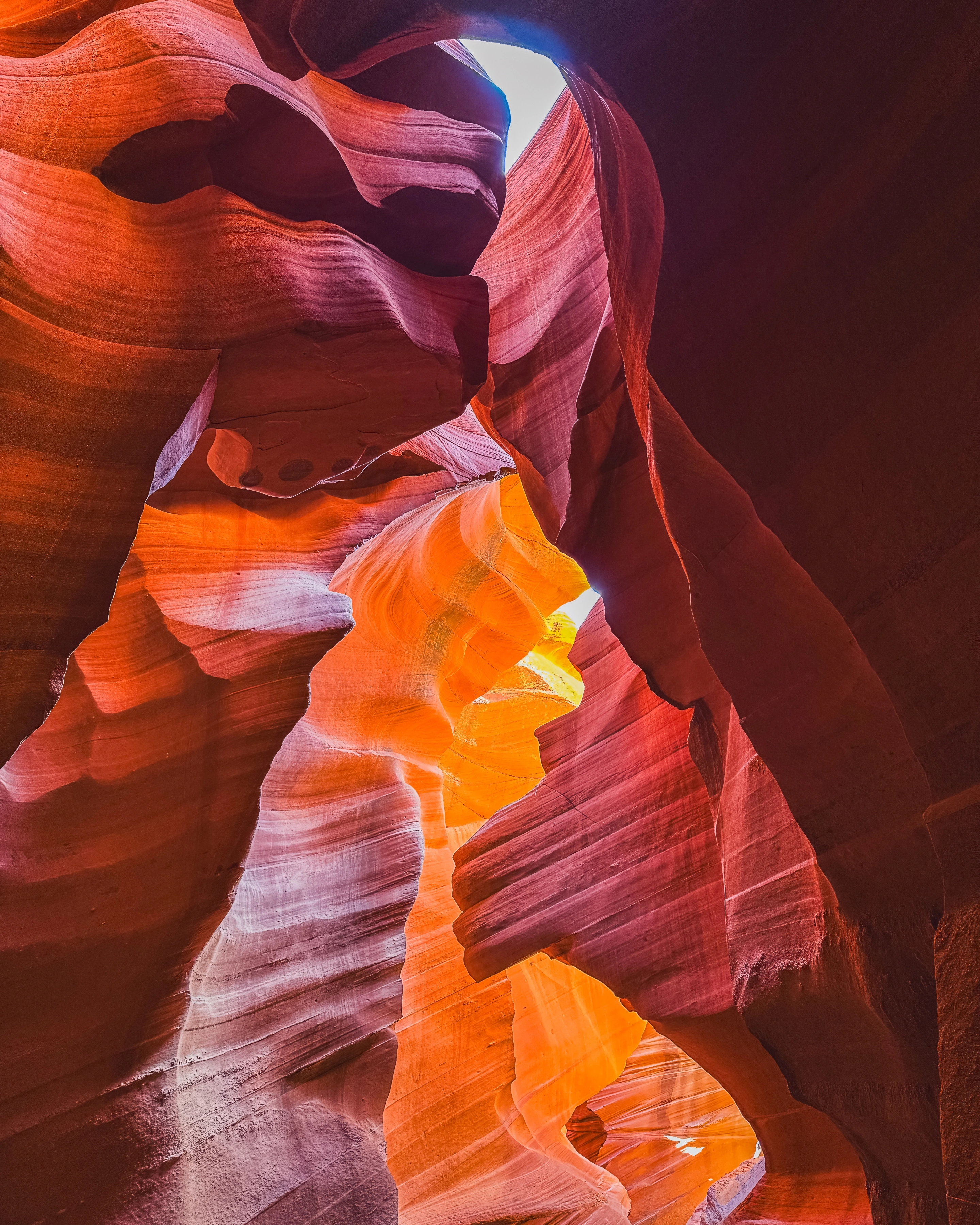 Orange, red and magenta rock walls curve around a narrow bright opening and luminous channel.