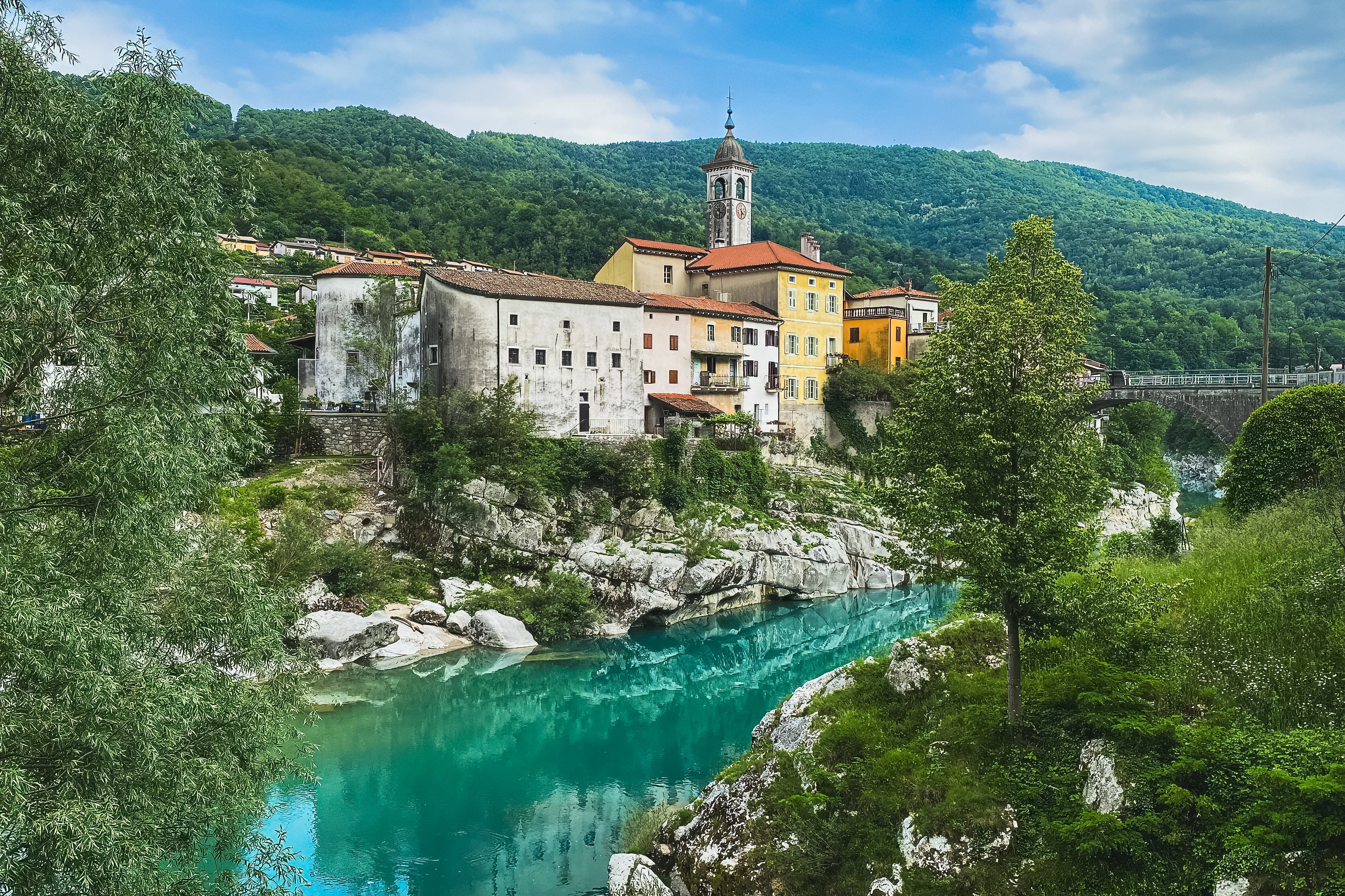 Pale and yellow buildings rise above turquoise water between trees and exposed rock.
