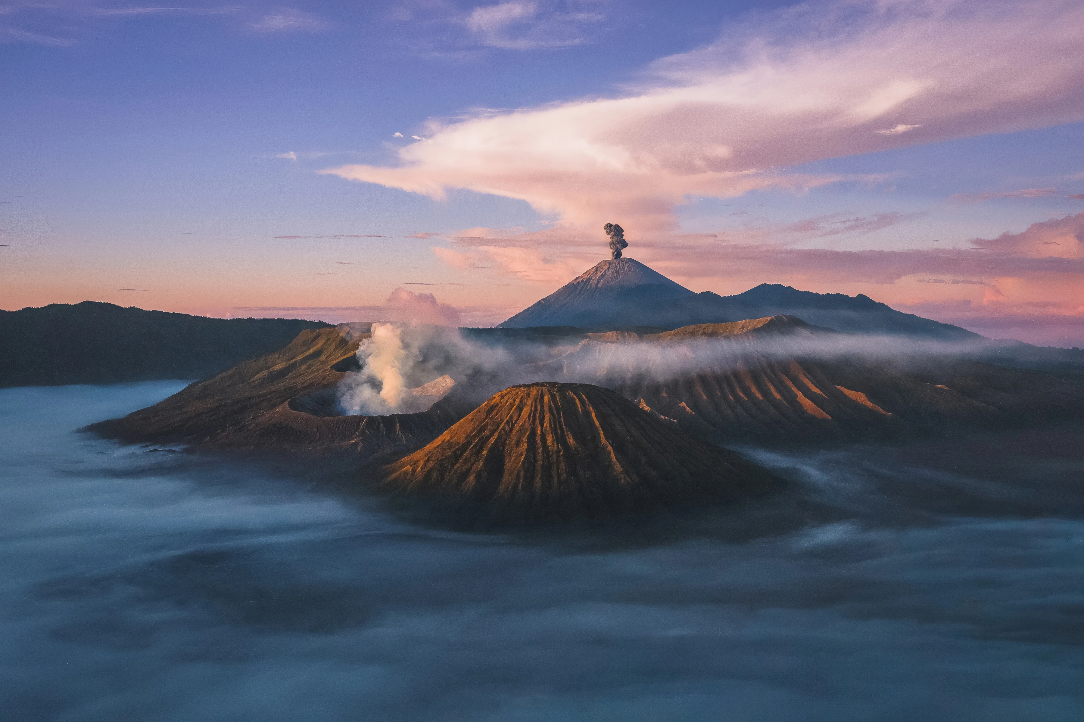 Volcanic cones and plumes rise from low mist beneath a warm sky.