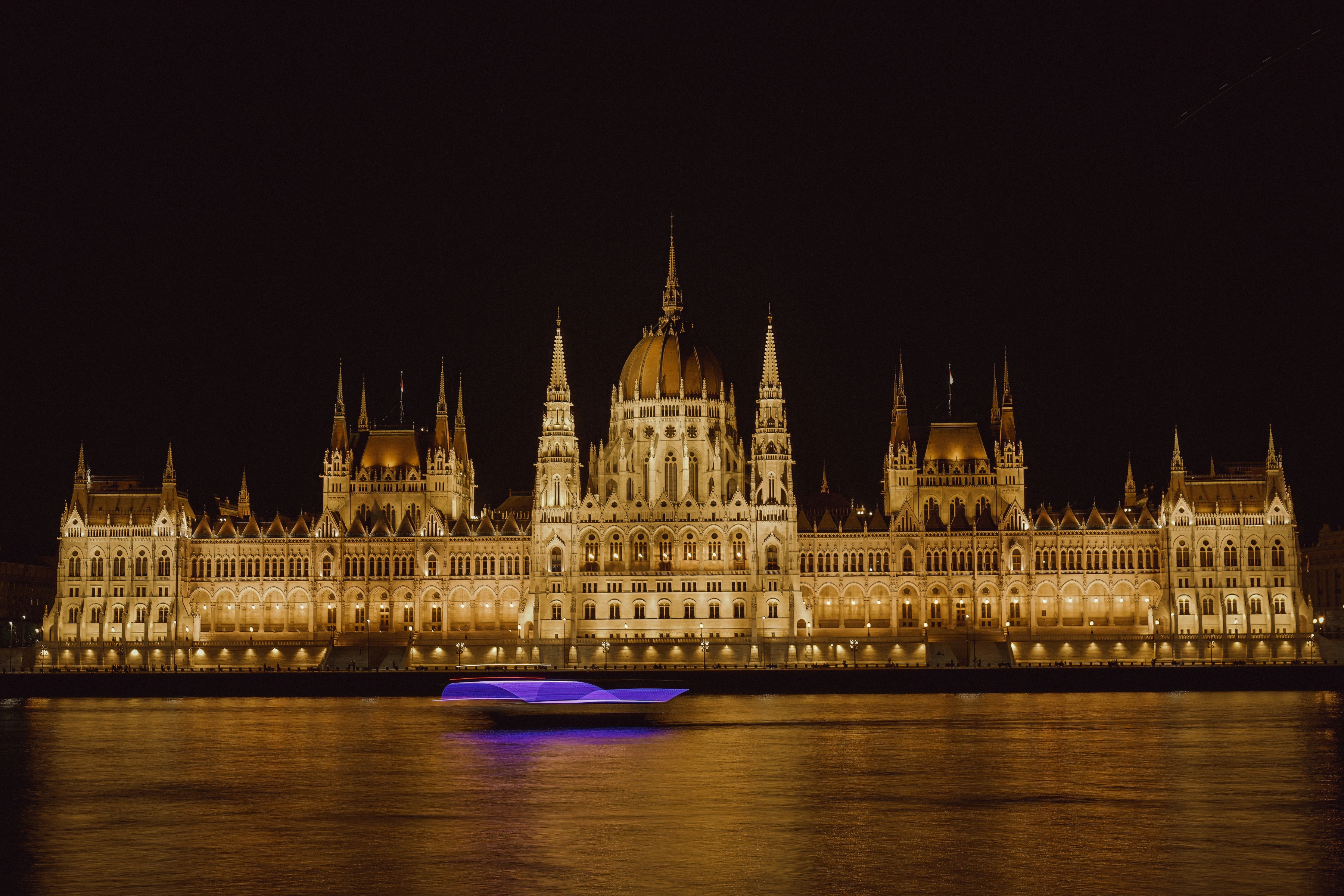 A moving boat leaves a purple light streak below an illuminated domed riverside building.