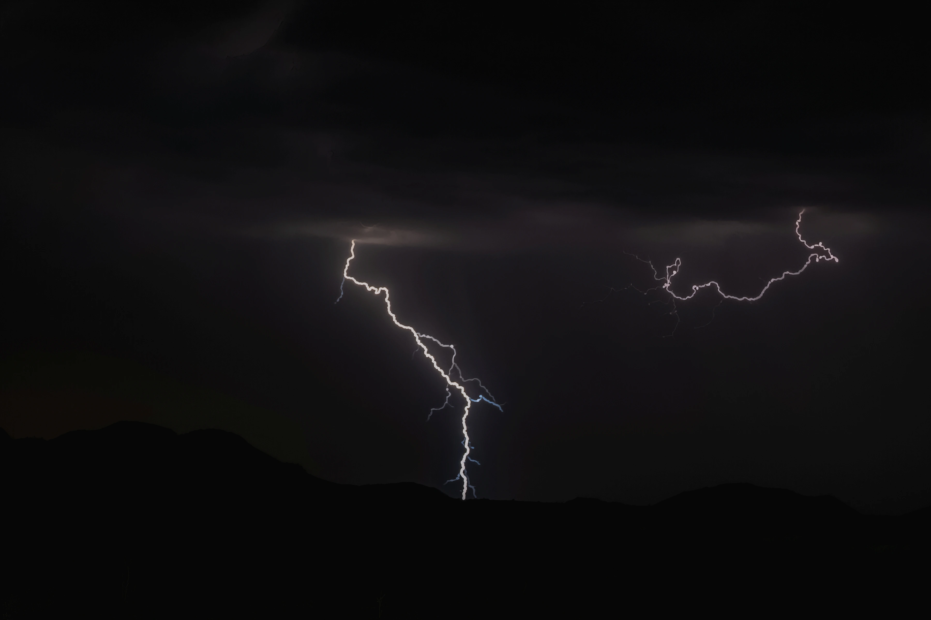 Branching lightning crosses a dark sky above a low ridge and faint vegetation.