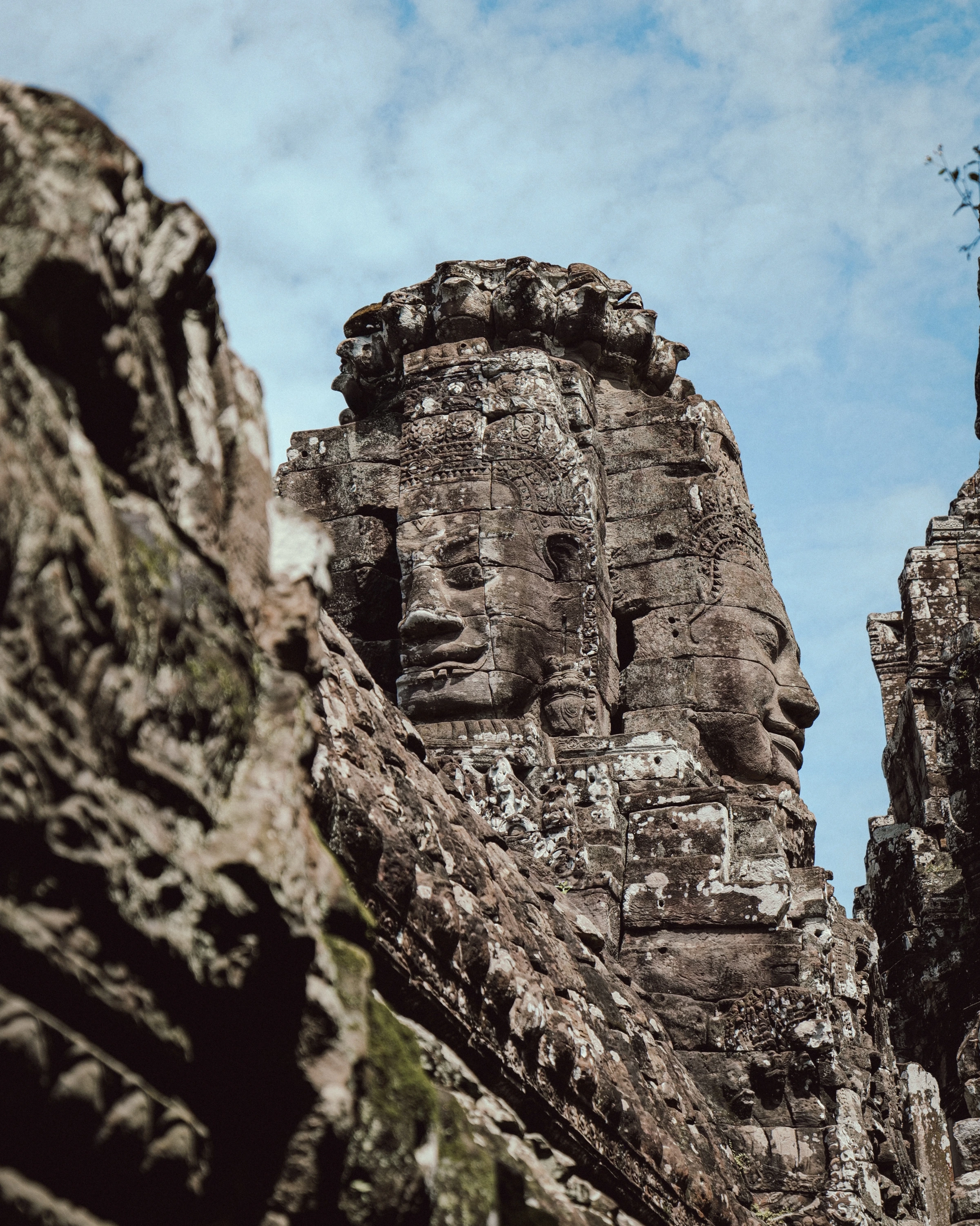 A carved stone tower shows a frontal face and another face in profile, partly framed by softer foreground stone.