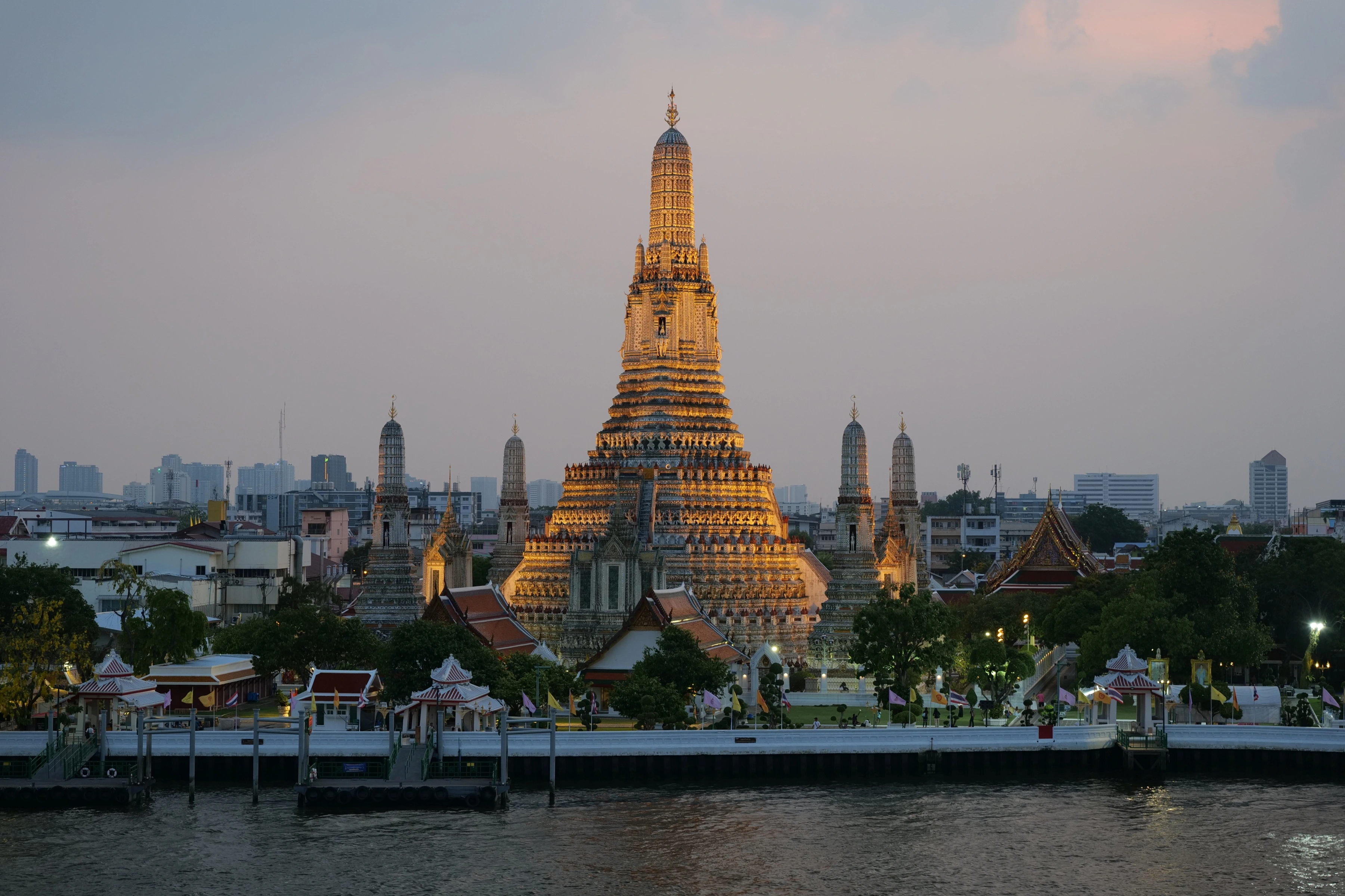 A warm-lit ornate tower rises above riverside buildings, smaller towers and a distant modern skyline.