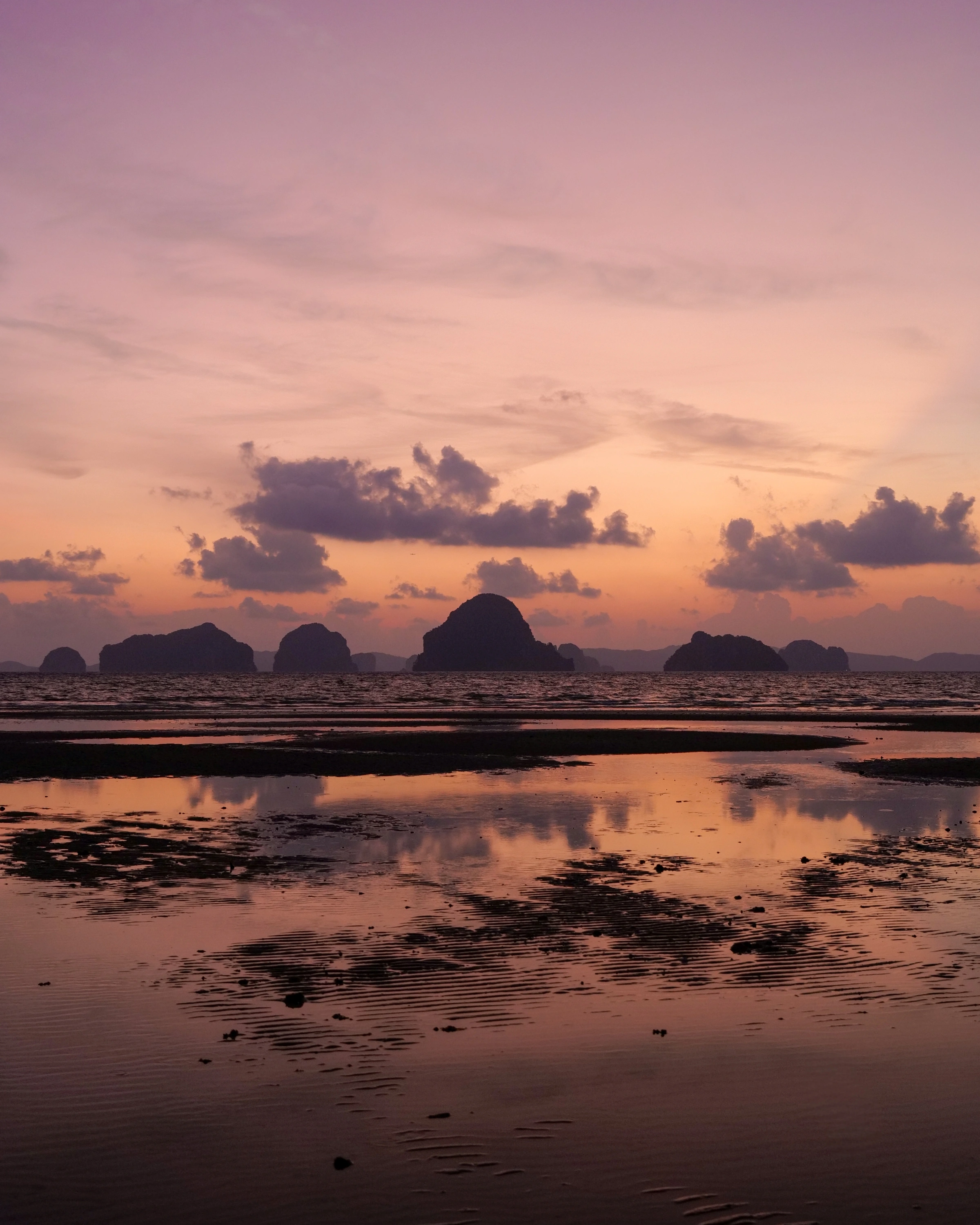 Rocky island silhouettes sit above wet-sand reflections beneath a pink and orange sky.