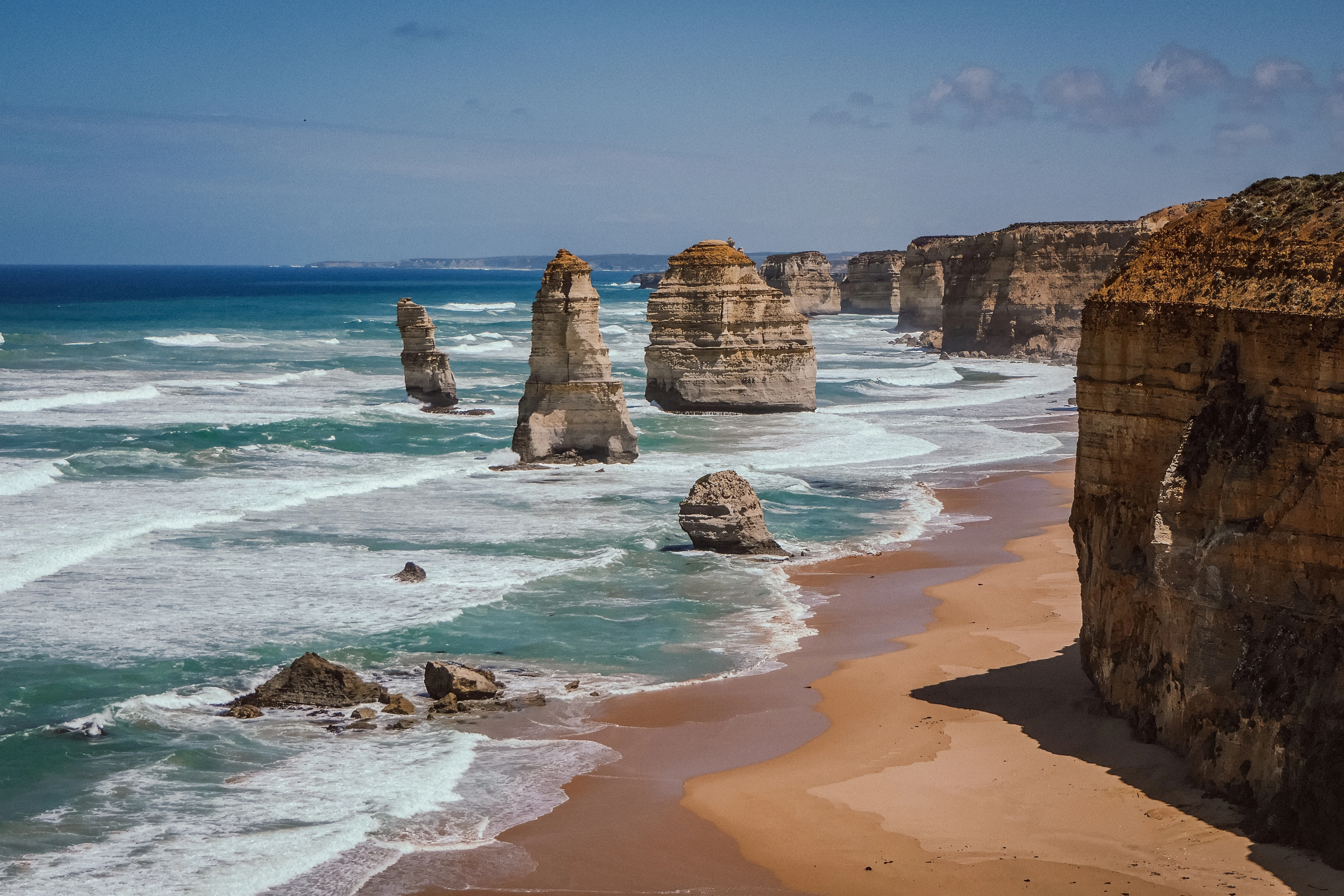 Rock stacks rise from breaking surf beside a receding cliff and beach.