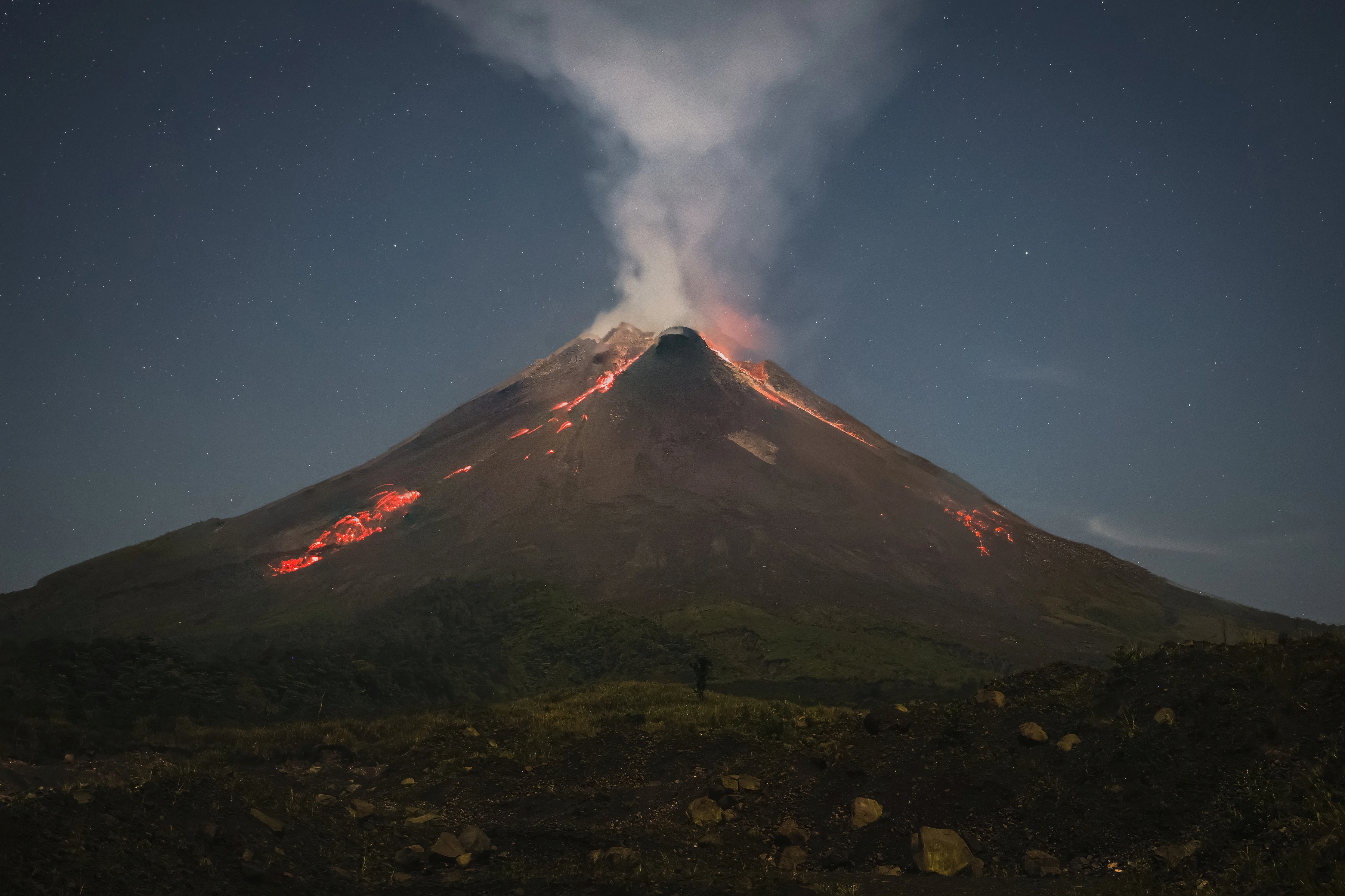 Glowing red streaks mark a volcanic cone beneath a rising plume and stars.