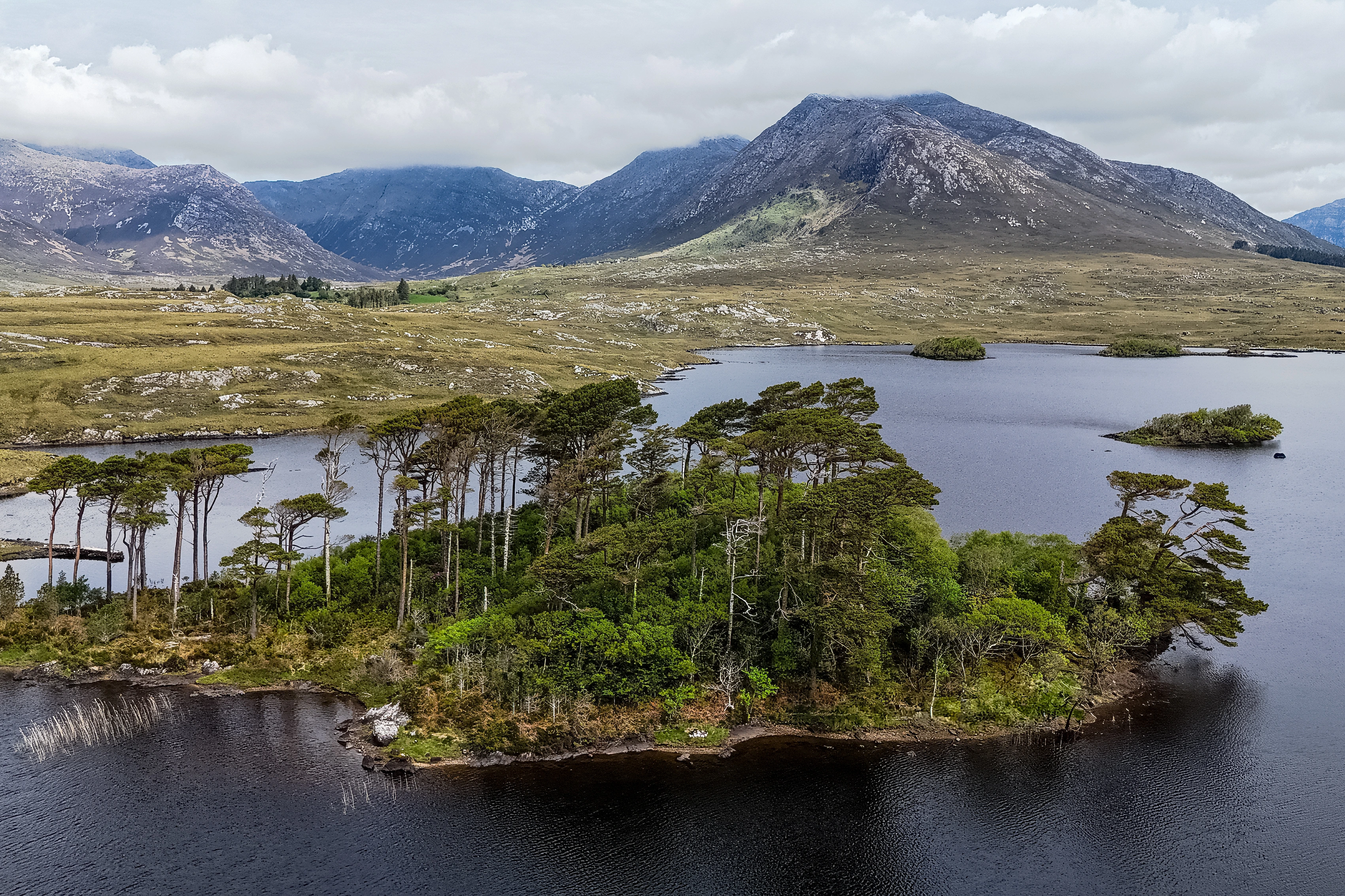 A tree-covered landform extends into calm water below mountain slopes.