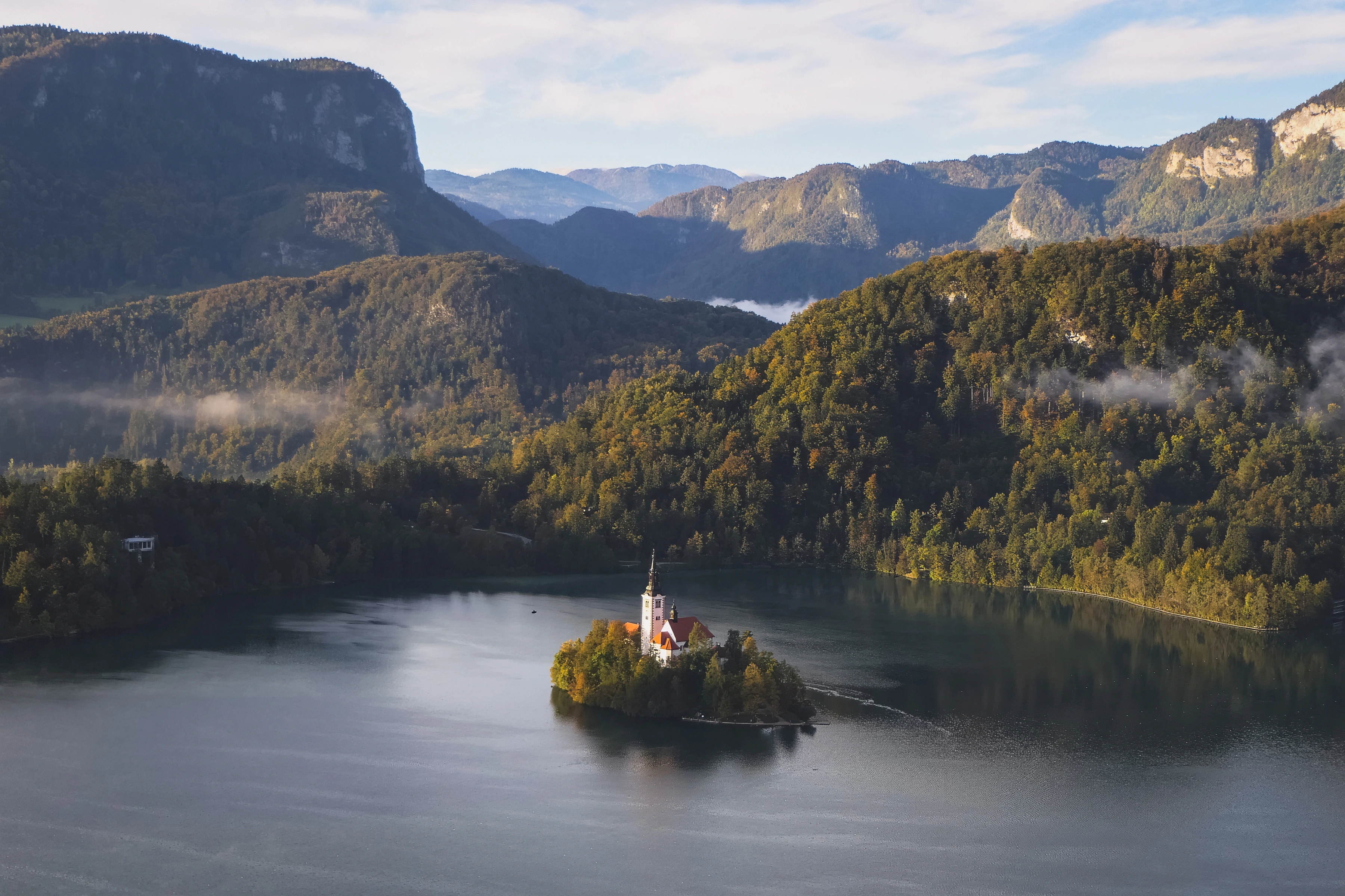 A church on a small lake island sits below wooded hills and low mist.